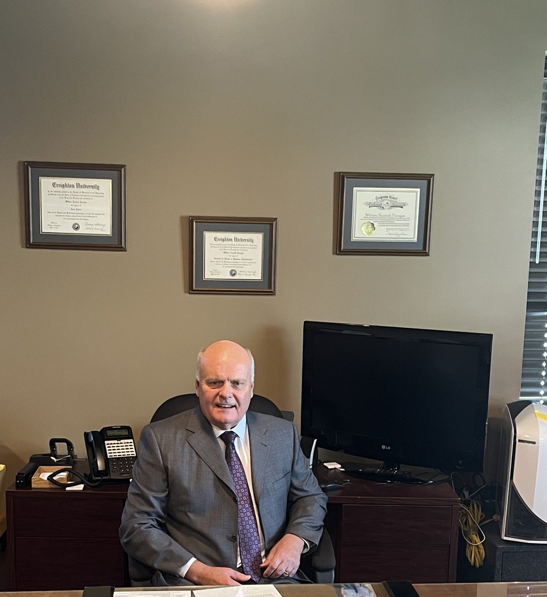 Jim Bachman at his desk beneath his framed Creighton law and accounting degrees.